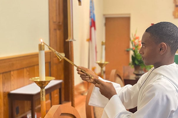Student altar server lighting candle in chapel during service.