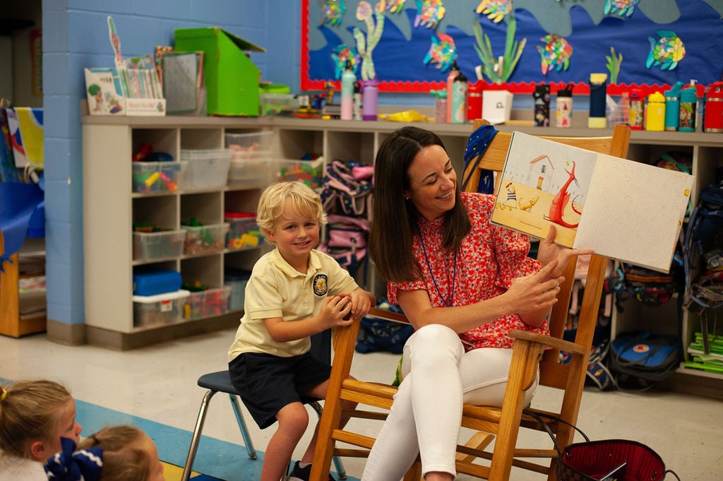 A teacher reading a book with a student sitting next to her.