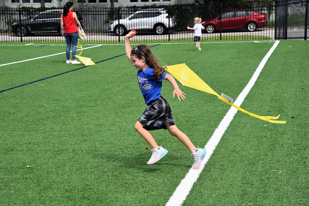 Kindergarten student joyfully running outside on field with a kite.