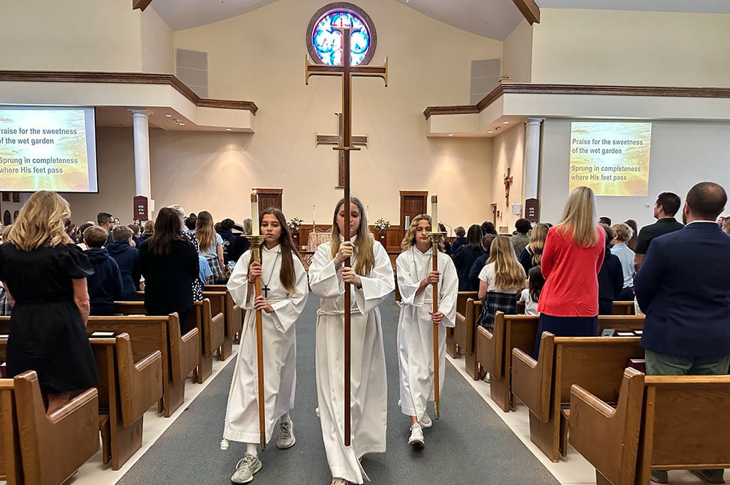 Altar servers walking down aisle with a cross and candles during church service.