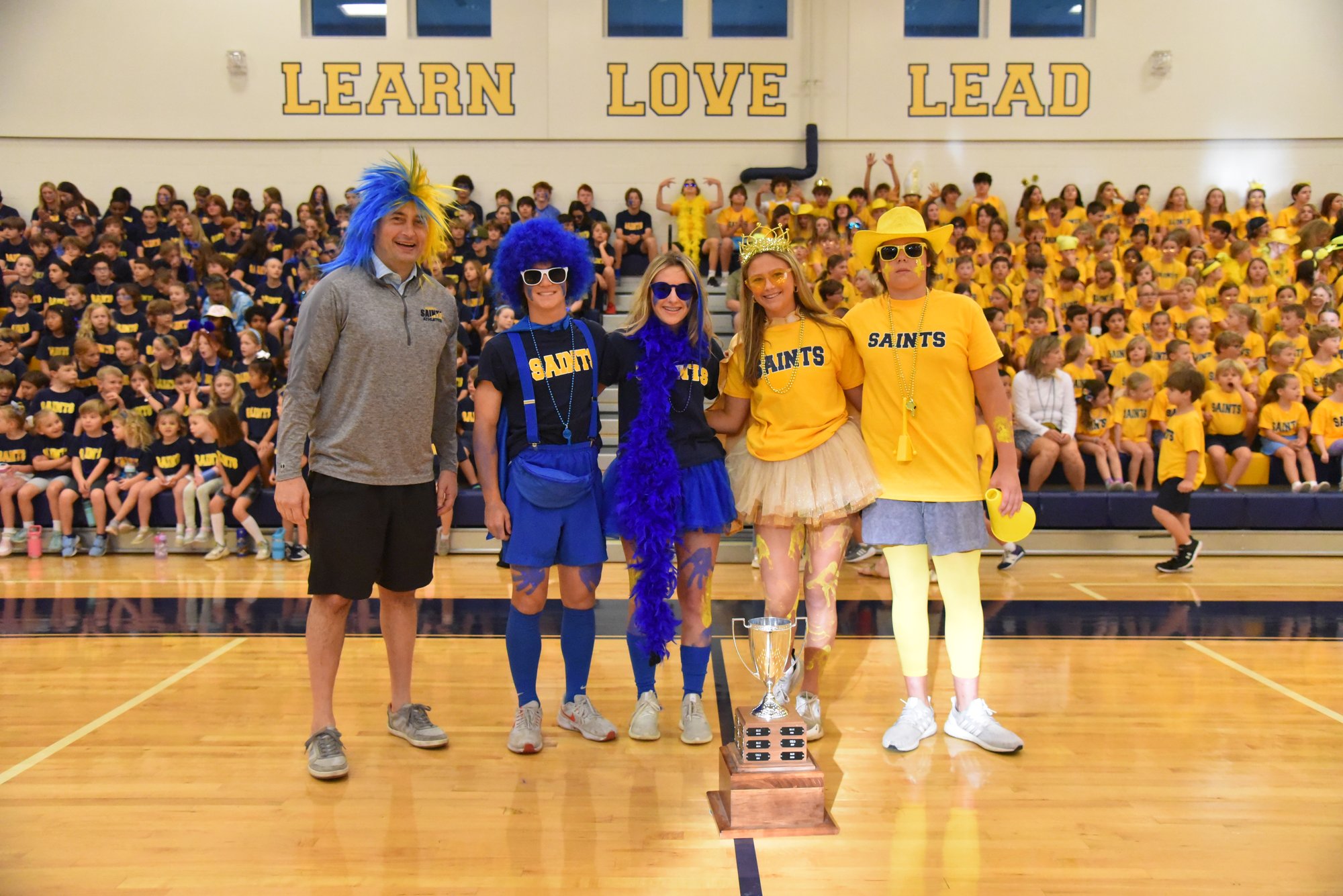 Students and faculty at a pep rally wearing costumes and wigs.