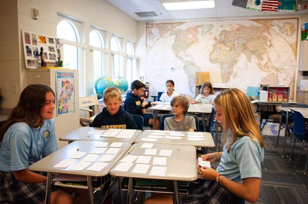 A group of students in desks doing a flashcard activity.
