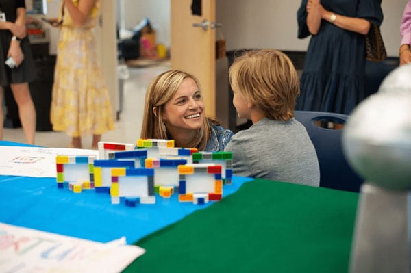 A teacher smiling at a student with the student's Lego activity in the foreground.