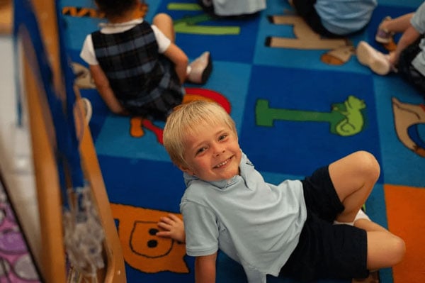 A child sitting down on an alphabet inspired rug.