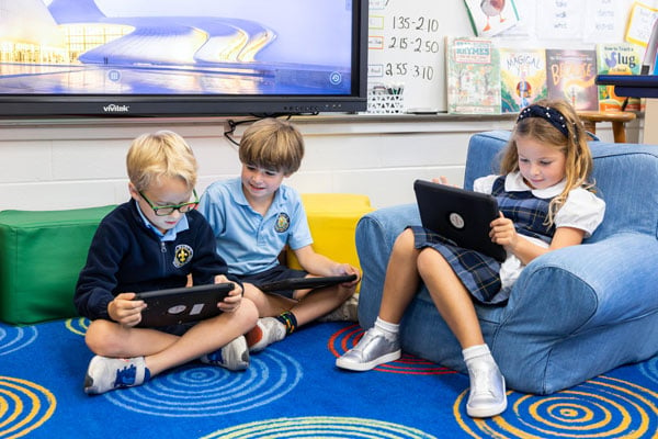 A group of students sitting on bean bag chairs reading on an iPad.