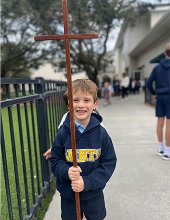 Student outside holding tall cross.